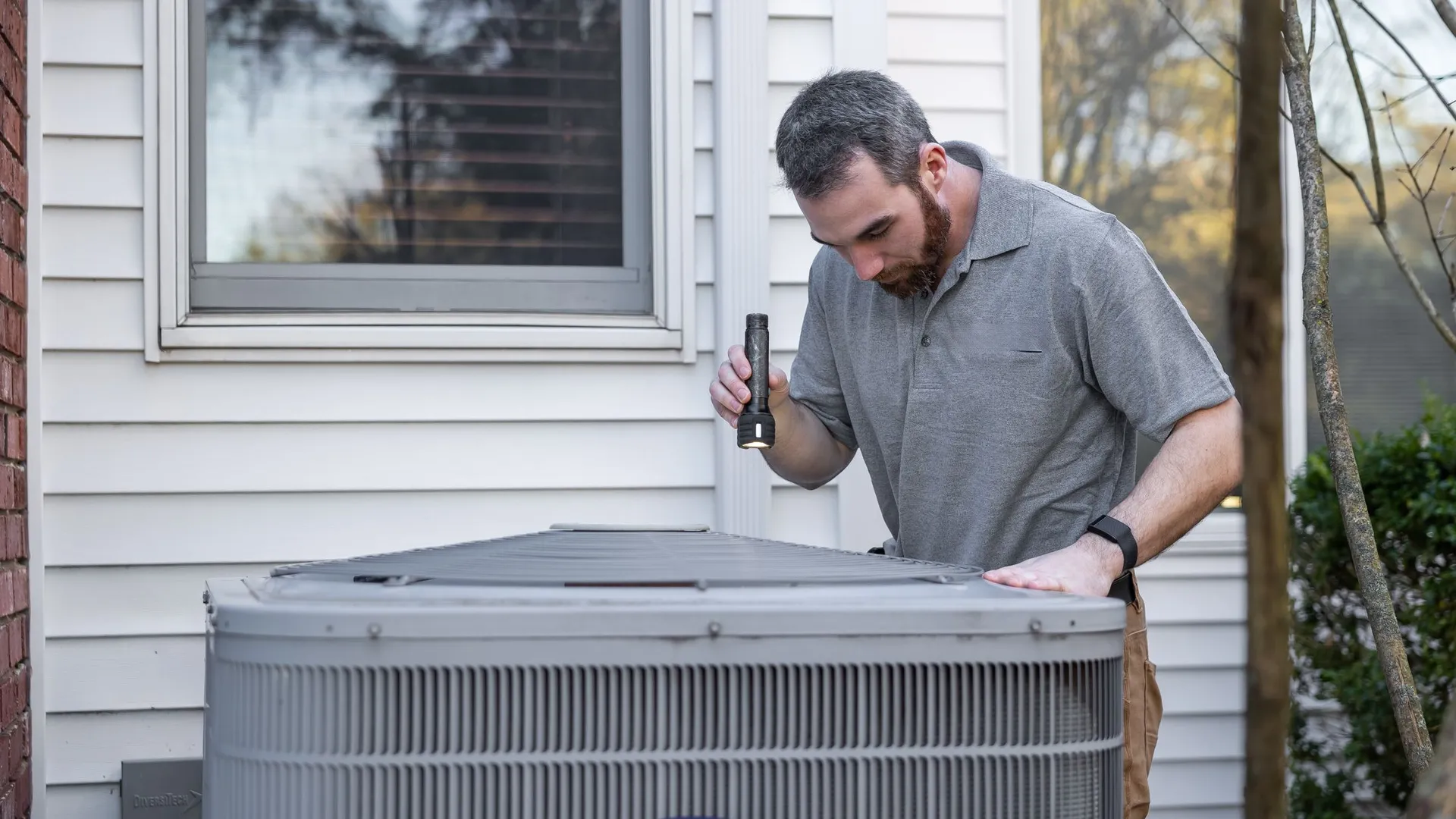 A technician checking an outdoor air conditioning unit beside a house